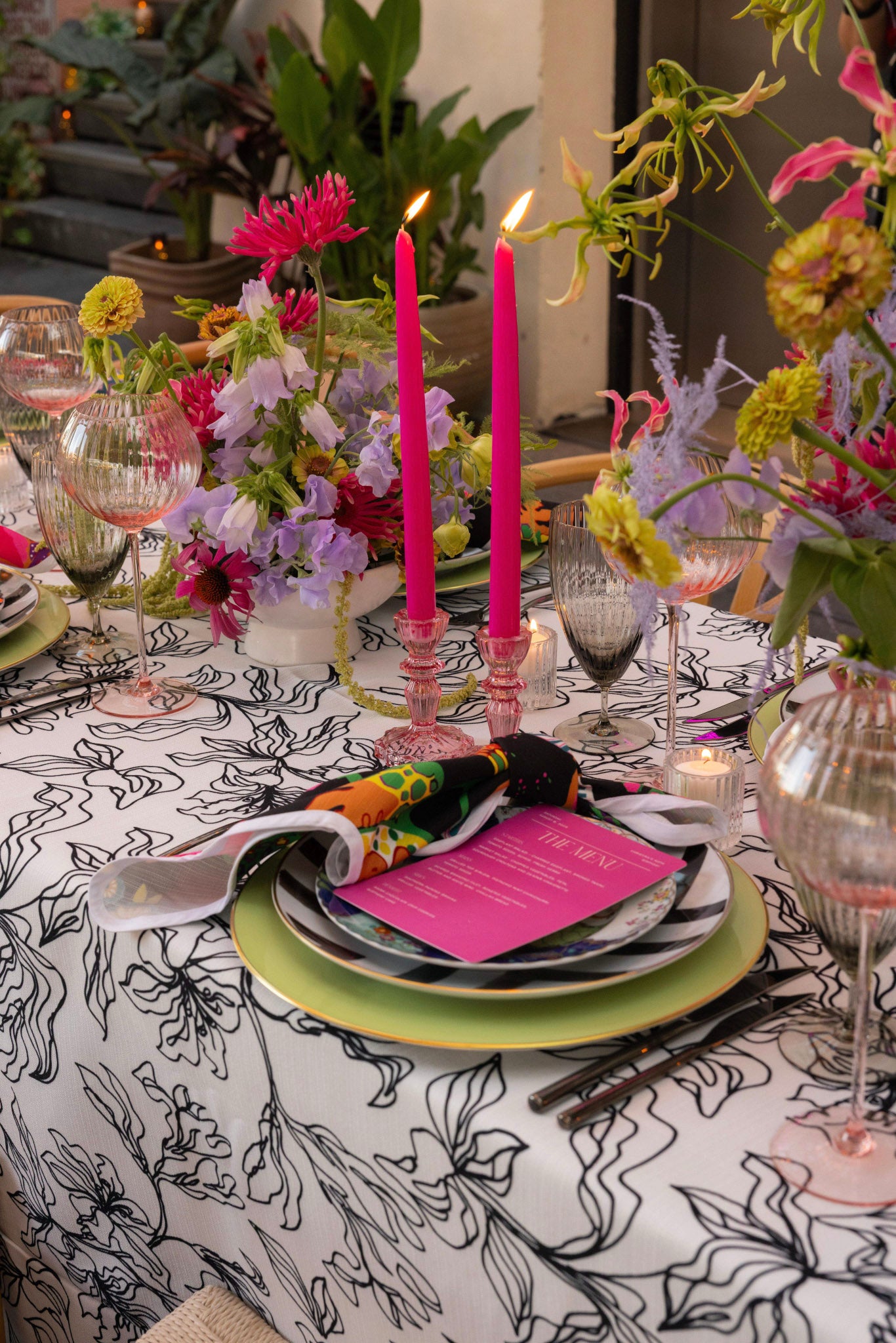 Decorative table setting with colorful flowers, candles, and patterned tablecloth.